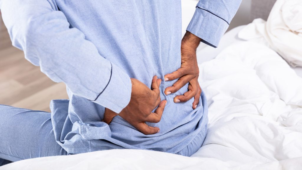 A person with a hand on their lower back, grimacing slightly