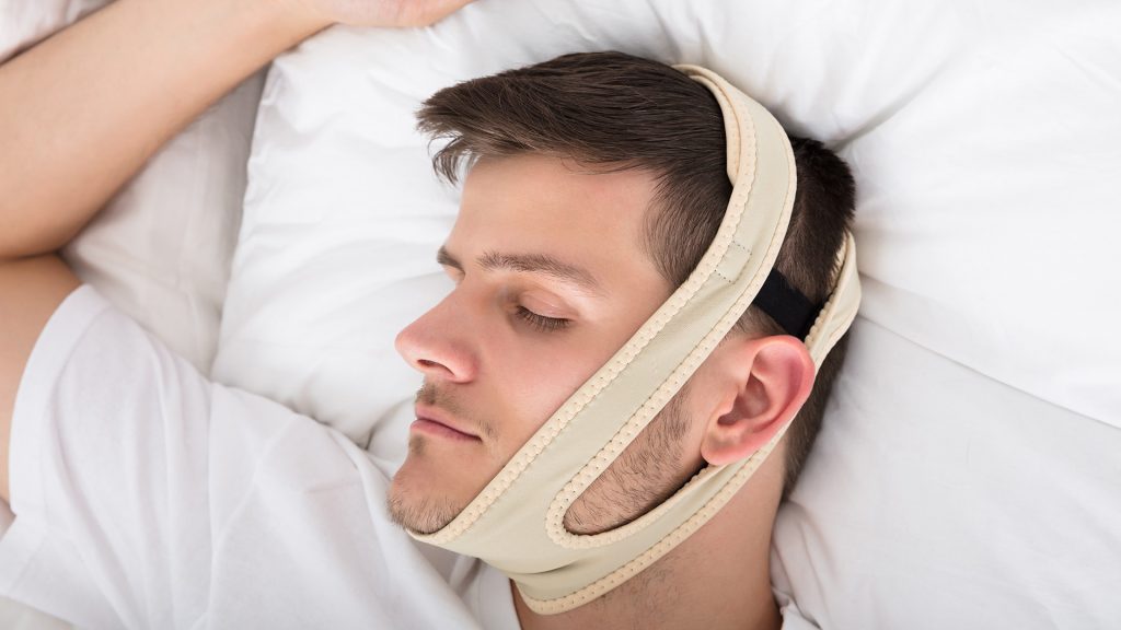 Close up of person sleeping in bed wearing a nasal strip or other visible anti-snoring device
